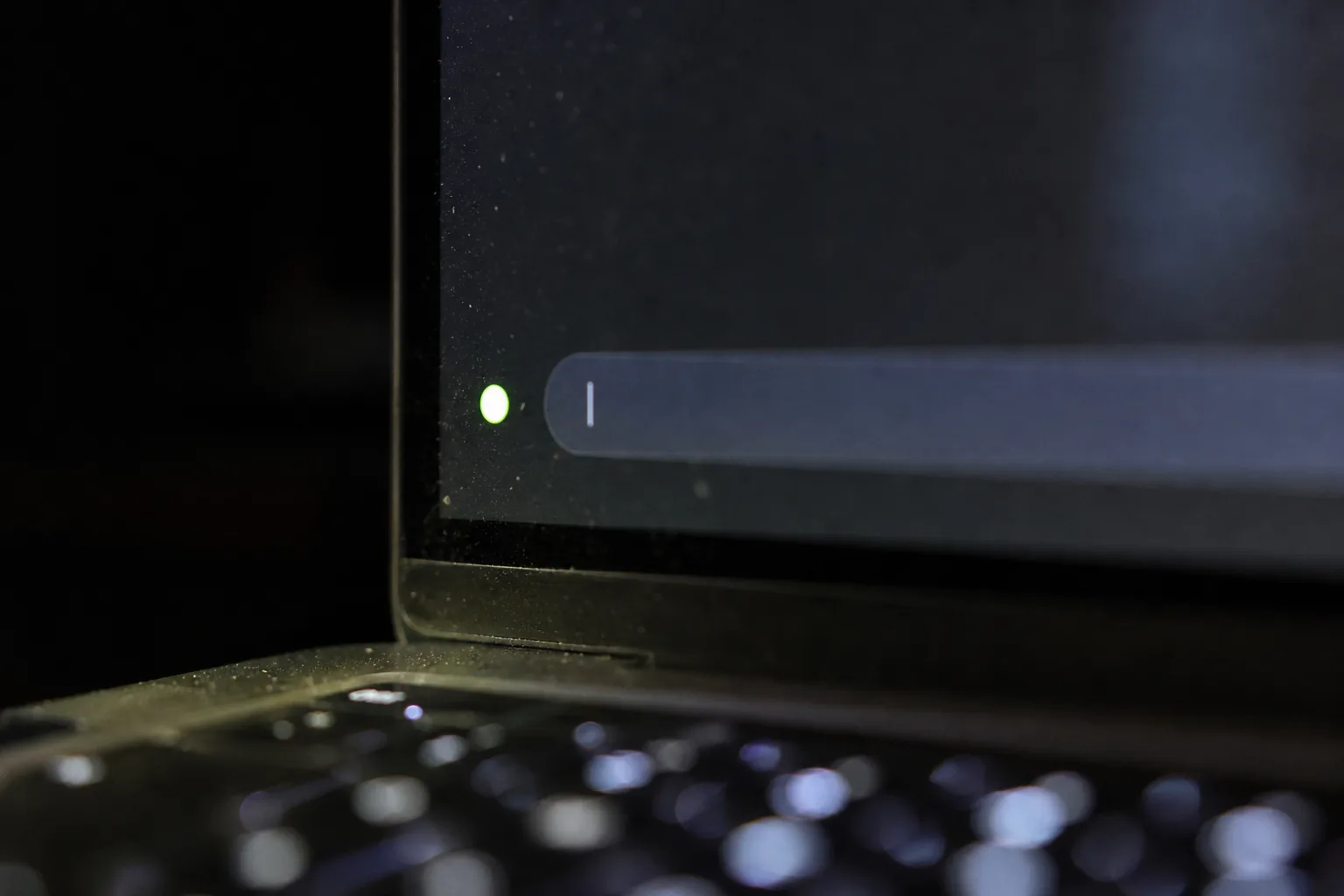 Close detail of a laptop screen edge with a text field, a blinking cursor and a small green recording dot